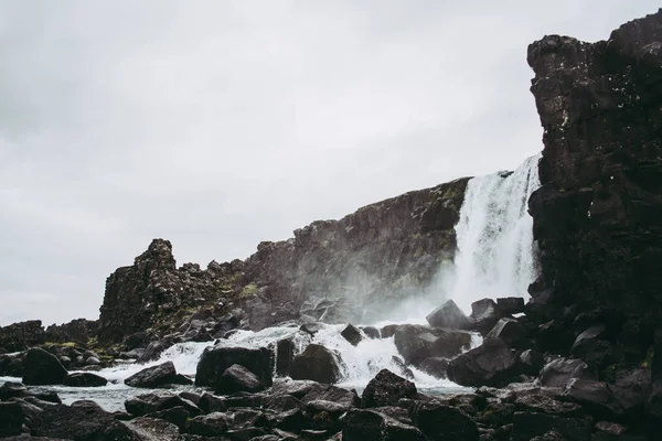 Wodospad w Parku Narodowym Thingvellir, Islandia płynie do basenu wypełnione kamieniami. Zimny deszcz na wiosnę — Zdjęcie stockowe