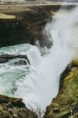 İzlanda Gullfoss şelale dikey görünümü. Kayalık dağlar arasında soluk beyaz sıçramalar