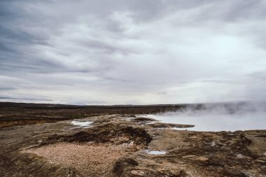 Sonsuz İzlanda manzaraları. Ufukta soluk beyaz gayzer buhar ve bulutlar