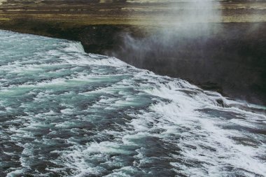 Siyah taşlar üzerinde akan ve şelale kenarından düşen beyaz köpük ile mavi su ile Dreamy İzlanda manzara