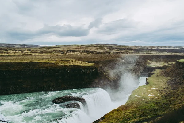 Campos verdes, rochas negras e água azul-turquesa da cachoeira Gullfoss na Islândia. Nuvens de salpicos voando no ar — Fotografia de Stock