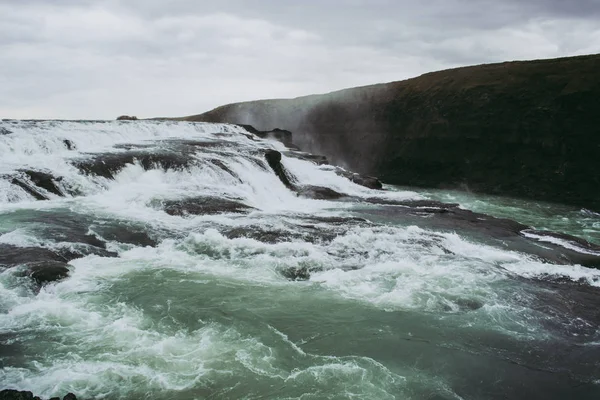 Cascade vattenfall på Island. Vita stänk, turkos vatten och svart sten under den grå himlen. Våren — Stockfoto