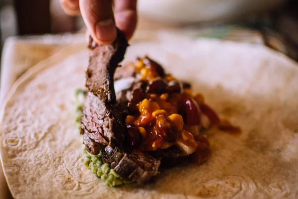Chief laying a piece of beef steak on burrito ingredients. Homemade burrito preparation process — Stock Photo, Image