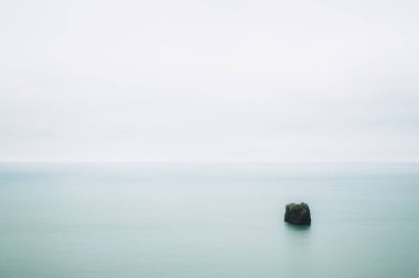 Atlantik okyanusunun pürüzsüz turkuaz suyu ve içinde küçük bir kaya parçası. Sakinlik ve minimalizm. Güney İzlanda