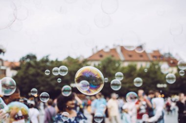 Renkli sabun kabarcıkları Prag, Çek Cumhuriyeti eski şehir üzerinde uçan. Ağaçlar ve binalar şeffaf kabarcıklar ile yansıtılır. Arka planda çok kültürlü turistler.