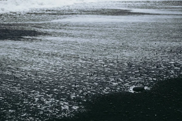 Biała piana wodna na czarnej piaszczystej plaży w Islandii — Zdjęcie stockowe