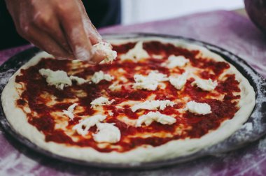 Bir erkek pizzaiolo mozzarella dilimlerini çiğ çiğ koyuyor.