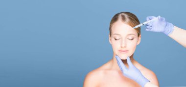 Genç ve güzel kadın cilt iğneleri mavi arka plan üzerinde sahip. Plastik cerrahi kavramı.