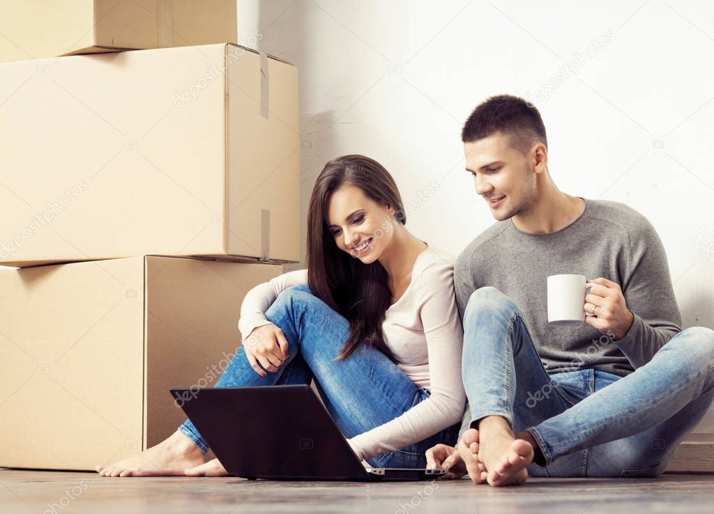 Man and woman with notebook computer and a boxes.  Young couple browsing internet with a laptop.  Moving in a new home concept.