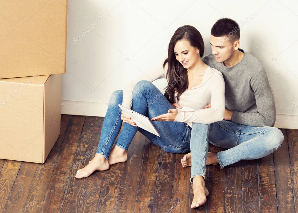 Man and woman with tablet computer and  boxes.  Young couple browsing internet with.  Moving in a new home concept.