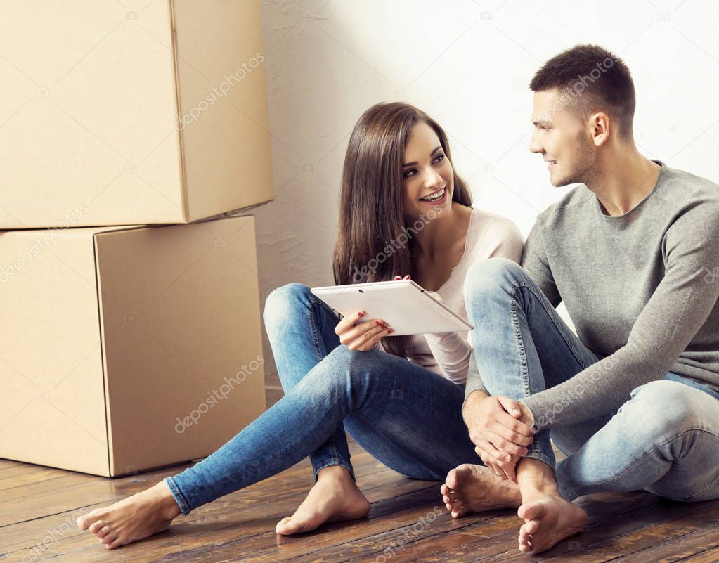 Man and woman with tablet computer and a boxes.  Young couple browsing internet with.  Moving in a new home concept.
