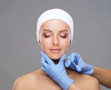 Genç bir kadının güzel yüzüne iğne yapan bir doktor. Estetik ameliyat, cilt gerdirme ve estetik tıp konsepti.