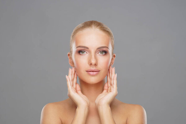 Beautiful face of young and healthy girl over grey background. Skin care, cosmetics and face lifting concept.
