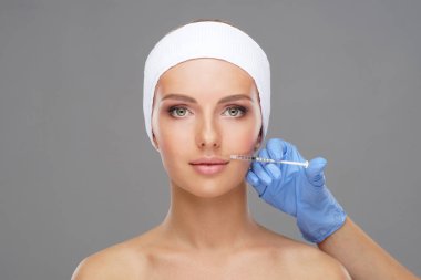 Genç bir kadının güzel yüzüne iğne yapan bir doktor. Estetik ameliyat, cilt gerdirme ve estetik tıp konsepti.