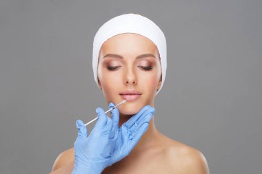 Genç bir kadının güzel yüzüne iğne yapan bir doktor. Estetik ameliyat, cilt gerdirme ve estetik tıp konsepti.