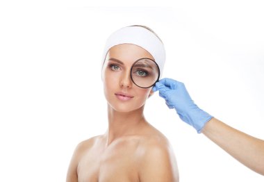 Genç ve güzel kız ve a magnifying cam yüz. Plastik cerrahi, yüz germe ve estetik tıp kavramı.