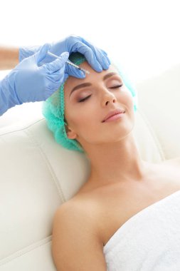 Genç bir kadının güzel yüzüne iğne yapan bir doktor. Estetik ameliyat, cilt gerdirme ve estetik tıp konsepti.