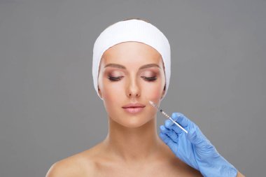 Genç bir kadının güzel yüzüne iğne yapan bir doktor. Estetik ameliyat, cilt gerdirme ve estetik tıp konsepti.