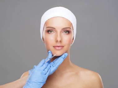 Genç bir kadının güzel yüzüne iğne yapan bir doktor. Estetik ameliyat, cilt gerdirme ve estetik tıp konsepti.
