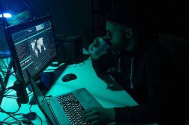 Bodrumdaki dizüstü bilgisayarları ve bilgisayarları kullanarak virüs fidye virüsü kodlamak için aranıyor. Siber saldırı, sistem kırma ve kötü amaçlı yazılım kavramı.