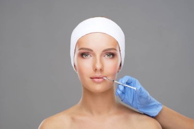 Genç bir kadının güzel yüzüne iğne yapan bir doktor. Estetik ameliyat, cilt gerdirme ve estetik tıp konsepti.