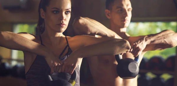 Fit, sporty and athletic people working in a gym using iron weights. Man and woman training with dumbbells. Sports, athletics and fitness concept.