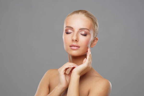 Beautiful face of young and healthy girl over grey background. Skin care, cosmetics and face lifting concept.