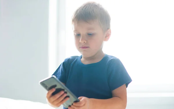 Portrait of happy boy playing with a smartphone. Kid with a mobile phone at home. Entertainment technology, futuristic gadgets, internet and generation Z concept. — Stock Photo, Image