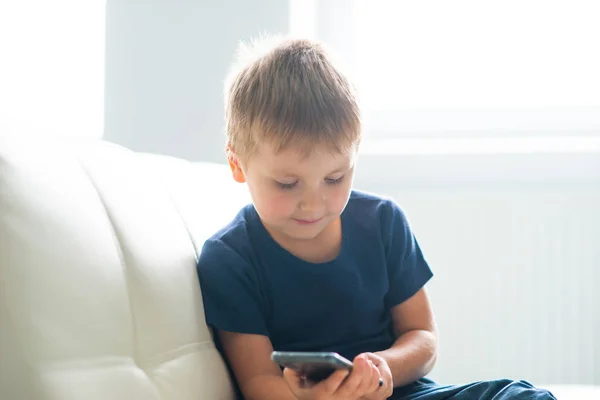 Portrait of happy boy playing with a smartphone. Kid with a mobile phone at home. Entertainment technology, futuristic gadgets, internet and generation Z concept. — Stock Photo, Image