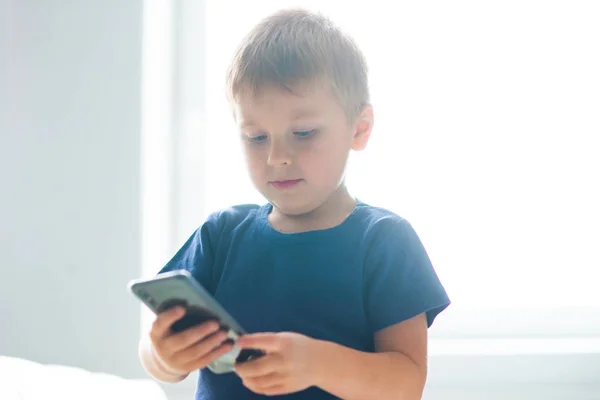 Portrait of happy boy playing with a smartphone. Kid with a mobile phone at home. Entertainment technology, futuristic gadgets, internet and generation Z concept. — Stock Photo, Image