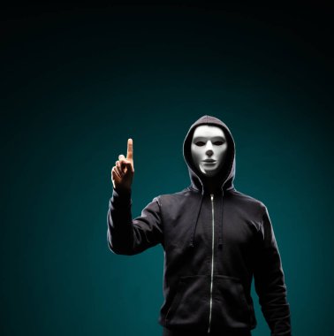 Bilgisayar korsanı beyaz maske ve kapüşonlu portresi. Gizlenmiş karanlık yüzü. Veri hırsız, internet dolandırıcılık, darknet ve siber güvenlik kavramı.
