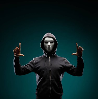 Bilgisayar korsanı beyaz maske ve kapüşonlu portresi. Gizlenmiş karanlık yüzü. Veri hırsız, internet dolandırıcılık, darknet ve siber güvenlik kavramı.