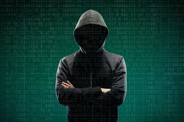 Computer hacker in mask and hoodie over abstract binary background. Obscured dark face. Data thief, internet fraud, darknet and cyber security concept.