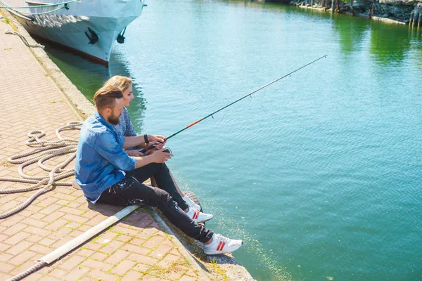 Man teaching his girlfriend to fishing. Couple with rod in harbor. Date, love and hobby concept.