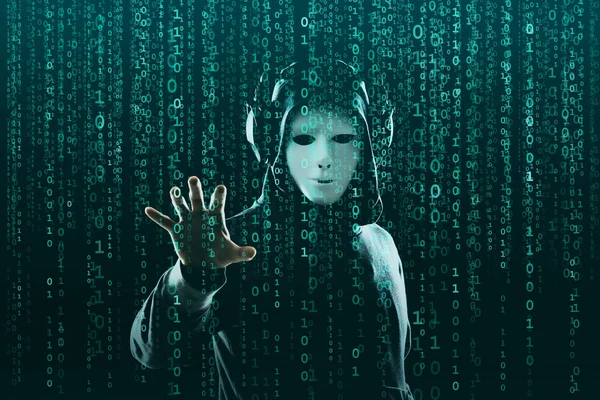 Computer hacker in mask and hoodie over abstract binary background. Obscured dark face. Data thief, internet fraud, darknet and cyber security concept.