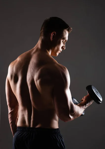 Strong, fit and sporty bodybuilder man with dumbbell over black background. Sport and fitness concept.