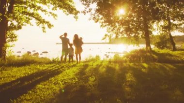 Mutlu bir aile denize yakın yürüyor. Kırsal kesimdeki tarla ve ağaçlar. Gün batımı veya gün doğumu sıcak renkler. Sevgi dolu ebeveynler ve güzel çocuklar. Aşk ve ebeveynlik kavramı.