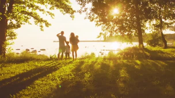 海の近くを歩く幸せな家族 田舎の野原と木々 日没や日の出の暖かい色 愛する両親と美しい子供たち 愛と親子の概念 — ストック動画