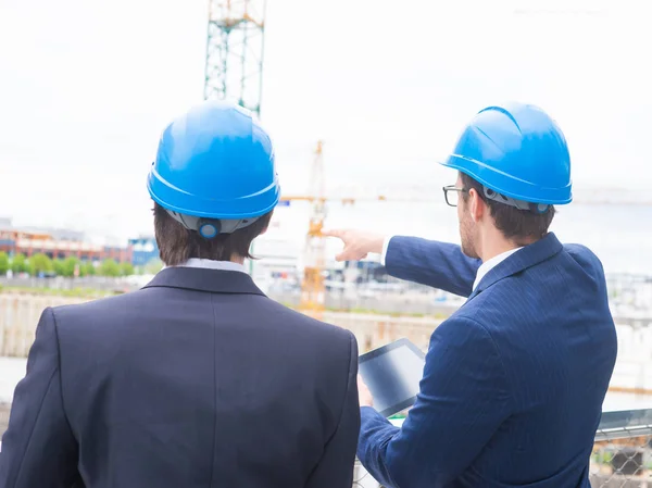 Real estate developers in helmets. New office construction. Confident business men and architect talking in front of modern office building. Businessman and his colleague have conversation.