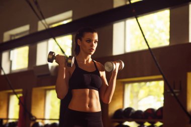 Spor salonunda çalışan fit, sportif ve atletik sporcu. Dambıl kullanan kadın eğitimi. Spor, yaşam tarzı, atletizm ve fitness konsepti.