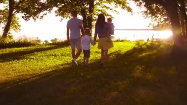 Mutlu bir aile denize yakın yürüyor. Kırsal kesimdeki tarla ve ağaçlar. Gün batımı veya gün doğumu sıcak renkler. Sevgi dolu ebeveynler ve güzel çocuklar. Aşk ve ebeveynlik kavramı.