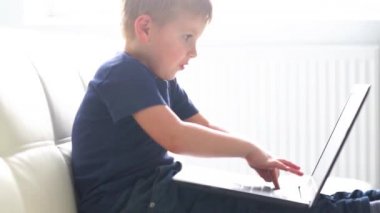 Bilgisayarla oynayan mutlu çocuğun portresi. Evde dizüstü bilgisayarı olan bir çocuk. Eğlence teknolojisi, fütüristik gadget'lar, internet ve nesil Z kavramı.