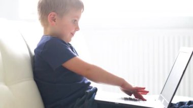 Bilgisayarla oynayan mutlu çocuğun portresi. Evde dizüstü bilgisayarı olan bir çocuk. Eğlence teknolojisi, fütüristik gadget'lar, internet ve nesil Z kavramı.