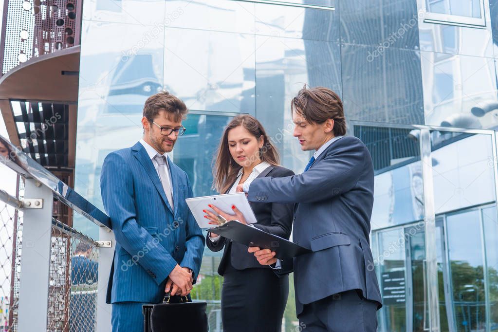 Confident businesspersons talking in front of modern office building. Businessmen and businesswoman have business conversation. Banking, professional job and financial market concept.