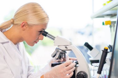 Tıp doktoru araştırma laboratuarında çalışıyor. Bilim asistanı ilaç deneyi yapıyor. Laboratuar araçları: mikroskop, test tüpleri, ekipman. Kimya, tıp, biyokimya, biyoteknoloji ve