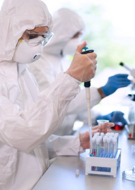 Laboratuvarda çalışan koruyucu giysi ve maskeli bilim adamları laboratuvar ekipmanları kullanıyorlardı: mikroskop, test tüpleri. İlaç, enfeksiyon ve aşı keşfi kavramı.