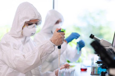 Scientists in protection suits and masks working in research lab using laboratory equipment: microscopes, test tubes. Biological hazard, pharmaceutical discovery, bacteriology and virology concept. clipart