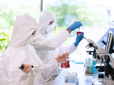 Laboratuvarda çalışan koruyucu giysi ve maskeli bilim adamları laboratuvar ekipmanları kullanıyorlardı: mikroskop, test tüpleri. İlaç, enfeksiyon ve aşı keşfi kavramı.