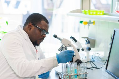 Laboratuvarda çalışan Afrikalı-Amerikalı bilim adamı. Doktor mikrobiyoloji araştırması yapıyor. Laboratuvar aletleri: mikroskop, test tüpleri, ekipmanlar. Biyoteknoloji, kimya, bakteriyoloji, virüs ve sağlık hizmetleri.