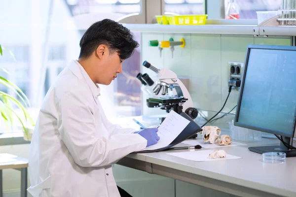 Azjatycki naukowiec pracujący w laboratorium. Lekarz prowadzący badania mikrobiologiczne. Narzędzia laboratoryjne: mikroskop, probówki, sprzęt. Biotechnologia, chemia, bakteriologia, wirusologia, DNA i opieka zdrowotna. — Zdjęcie stockowe